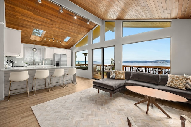 living room with wood ceiling, rail lighting, a water view, high vaulted ceiling, and light hardwood / wood-style flooring