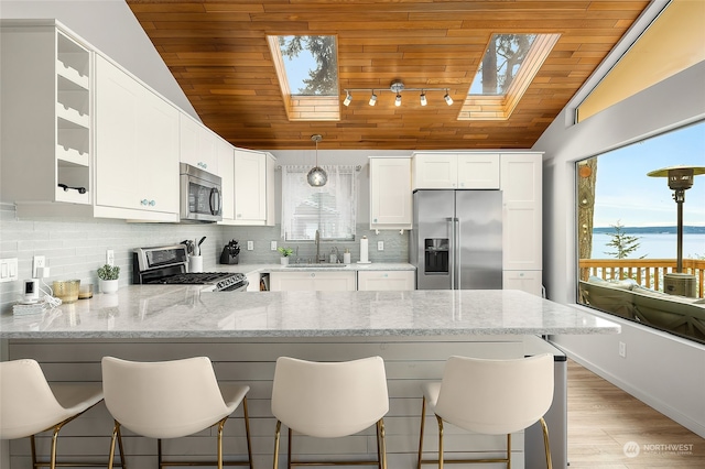 kitchen featuring a breakfast bar area, kitchen peninsula, light stone countertops, white cabinets, and appliances with stainless steel finishes