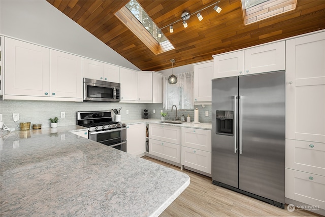 kitchen with hanging light fixtures, stainless steel appliances, backsplash, lofted ceiling with skylight, and white cabinets