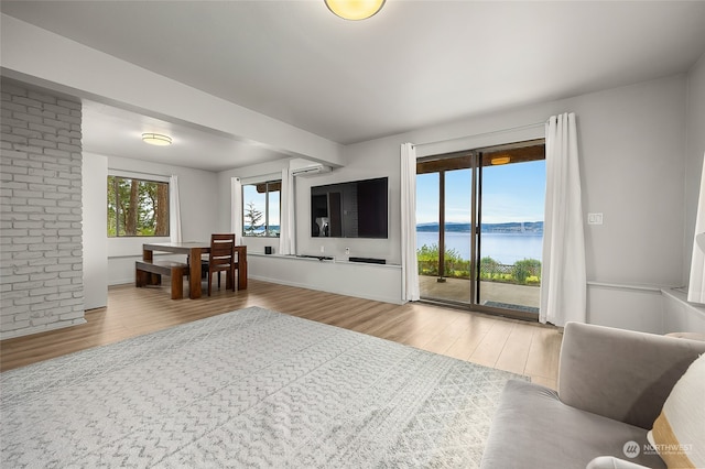 living room with a wall mounted air conditioner, a water view, and light hardwood / wood-style floors