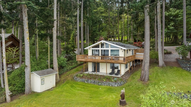 rear view of property featuring a yard, a storage unit, a wooden deck, and a patio