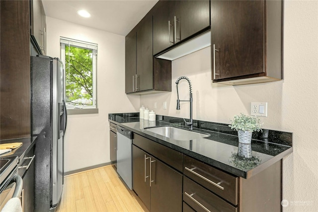 kitchen with dark brown cabinets, stainless steel appliances, dark stone countertops, sink, and light wood-type flooring