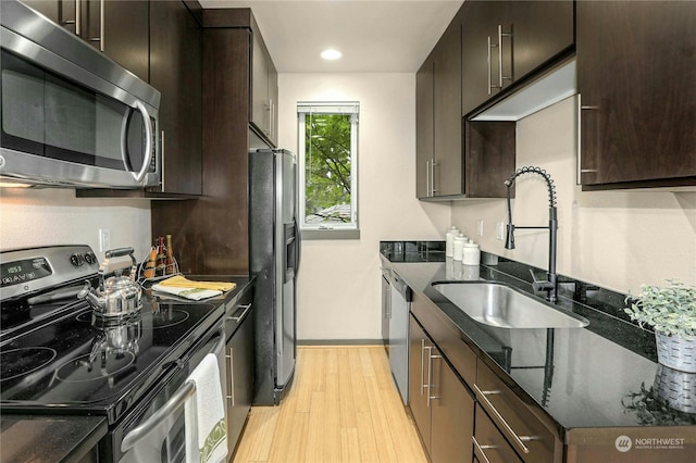 kitchen with appliances with stainless steel finishes, dark brown cabinetry, sink, and light hardwood / wood-style floors