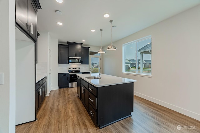 kitchen featuring sink, stainless steel appliances, light hardwood / wood-style flooring, pendant lighting, and a kitchen island with sink