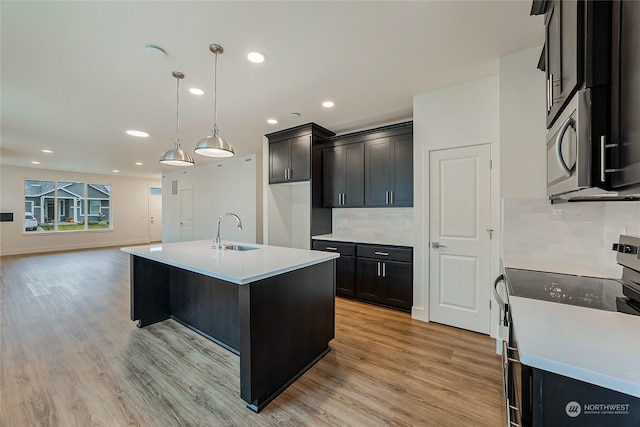 kitchen with a kitchen island with sink, hanging light fixtures, light wood-type flooring, appliances with stainless steel finishes, and tasteful backsplash