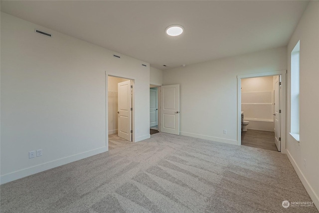 unfurnished bedroom with a walk in closet, connected bathroom, and light colored carpet