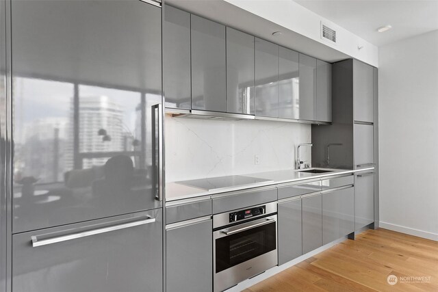 kitchen with sink, built in fridge, stainless steel oven, light hardwood / wood-style floors, and black electric cooktop