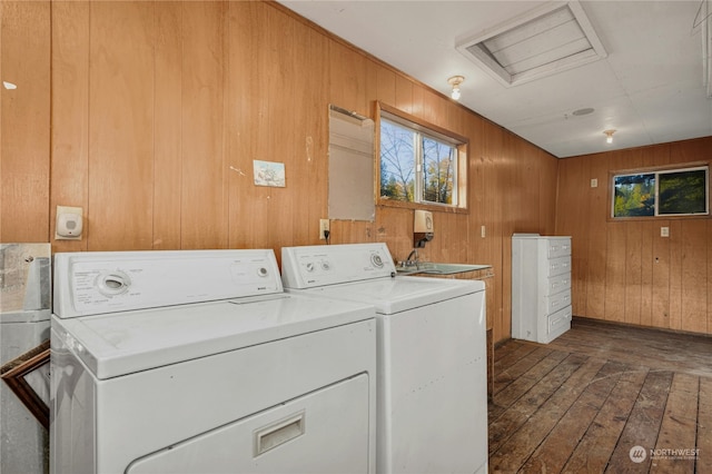 clothes washing area with dark wood-type flooring, washer and clothes dryer, wooden walls, and sink