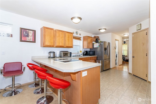 kitchen featuring a kitchen bar, kitchen peninsula, sink, and stainless steel refrigerator with ice dispenser