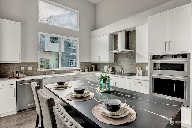 kitchen featuring appliances with stainless steel finishes, wall chimney exhaust hood, sink, and white cabinetry