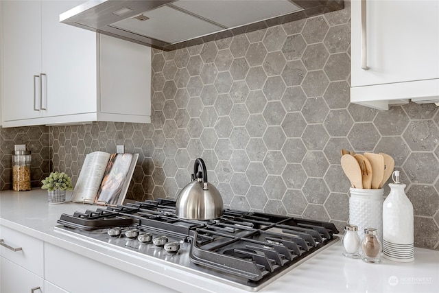 kitchen with tasteful backsplash, stainless steel gas cooktop, wall chimney range hood, and white cabinets