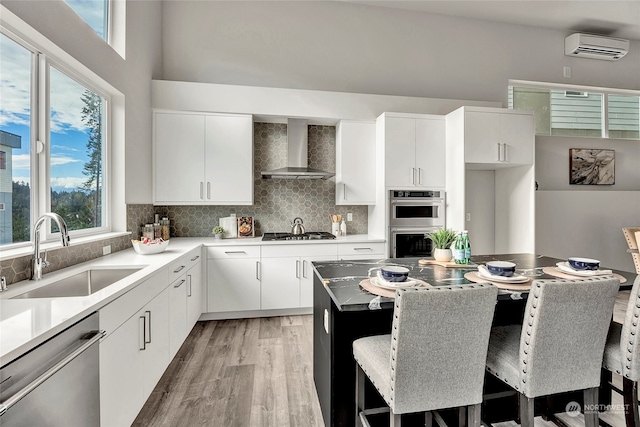 kitchen with a kitchen bar, sink, wall chimney range hood, and appliances with stainless steel finishes