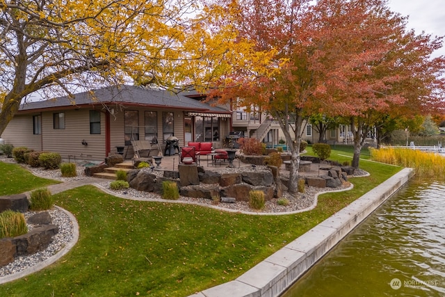 rear view of house with a water view, a patio, and a lawn