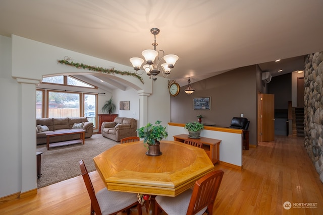 dining room with an AC wall unit, light hardwood / wood-style flooring, decorative columns, vaulted ceiling, and an inviting chandelier