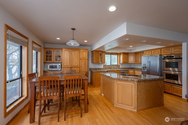 kitchen with a kitchen island, sink, decorative light fixtures, light wood-type flooring, and appliances with stainless steel finishes