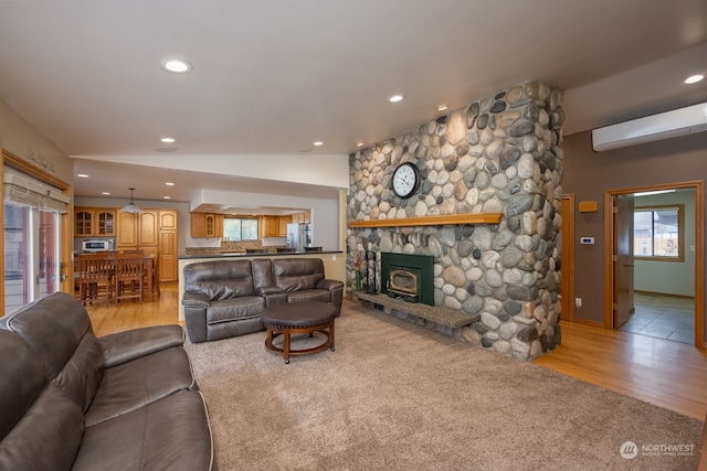 living room featuring an AC wall unit, vaulted ceiling, light wood-type flooring, and a stone fireplace