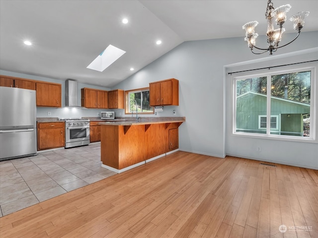 kitchen featuring kitchen peninsula, an inviting chandelier, light wood-type flooring, lofted ceiling with skylight, and appliances with stainless steel finishes