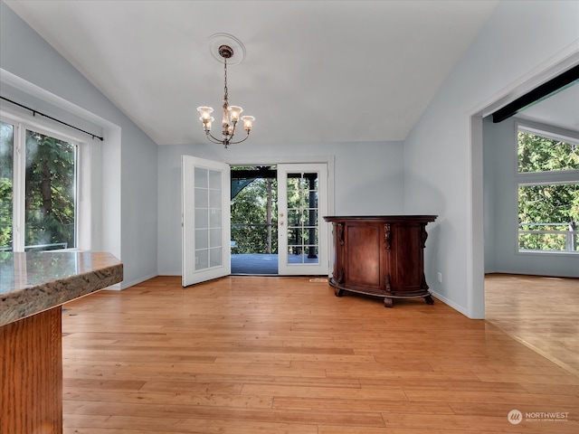 unfurnished dining area featuring light hardwood / wood-style floors, a chandelier, plenty of natural light, and vaulted ceiling