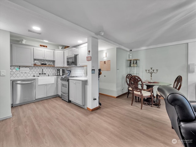 kitchen featuring appliances with stainless steel finishes, sink, light wood-type flooring, and decorative backsplash