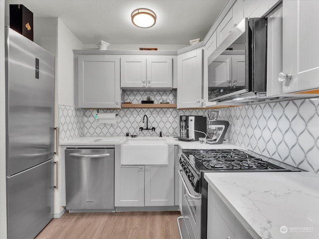 kitchen with stainless steel appliances, light stone countertops, light wood-type flooring, and decorative backsplash