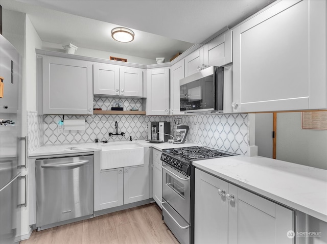 kitchen with white cabinetry, backsplash, stainless steel appliances, and light hardwood / wood-style flooring