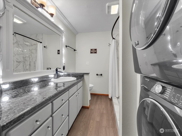 bathroom with toilet, stacked washing maching and dryer, wood-type flooring, a shower with shower curtain, and vanity