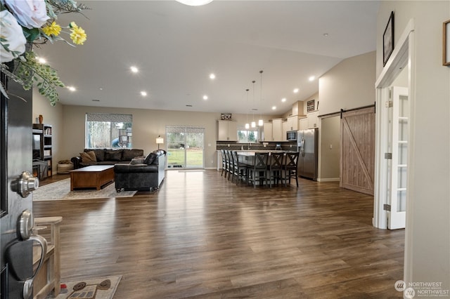 living room featuring a barn door, high vaulted ceiling, and dark hardwood / wood-style flooring