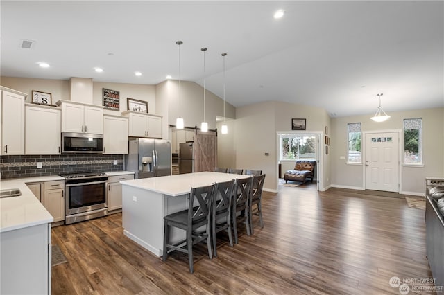 kitchen featuring vaulted ceiling, appliances with stainless steel finishes, hanging light fixtures, and a center island