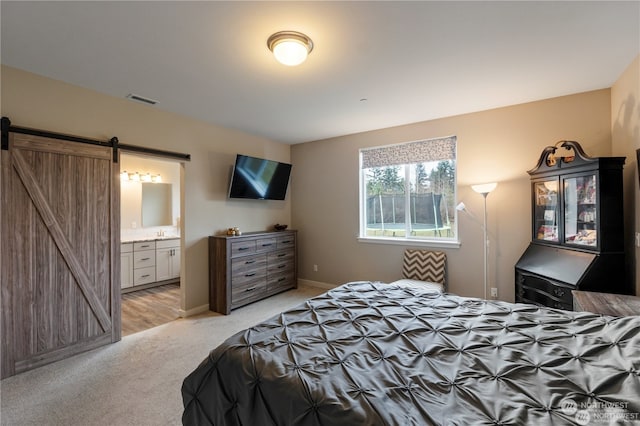 bedroom featuring sink, ensuite bath, a barn door, and light colored carpet