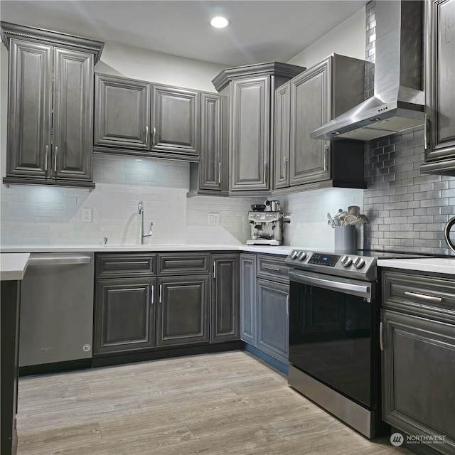 kitchen featuring wall chimney range hood, backsplash, appliances with stainless steel finishes, light hardwood / wood-style floors, and sink