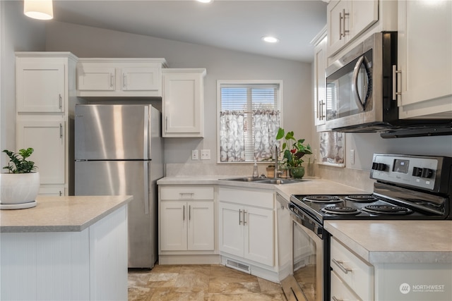 kitchen featuring appliances with stainless steel finishes, white cabinetry, sink, and vaulted ceiling