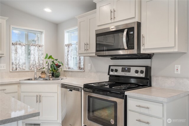 kitchen featuring appliances with stainless steel finishes, white cabinetry, sink, and vaulted ceiling