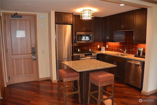 kitchen featuring light stone counters, a breakfast bar area, dark hardwood / wood-style flooring, stainless steel appliances, and a center island