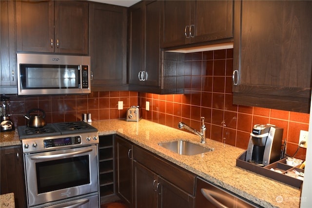 kitchen with backsplash, appliances with stainless steel finishes, light stone countertops, dark brown cabinetry, and sink