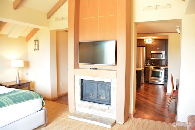 bedroom featuring a stone fireplace, light hardwood / wood-style flooring, and vaulted ceiling with beams