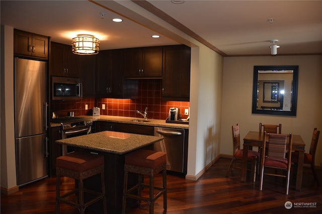 kitchen featuring a kitchen island, dark wood-type flooring, sink, a breakfast bar, and appliances with stainless steel finishes