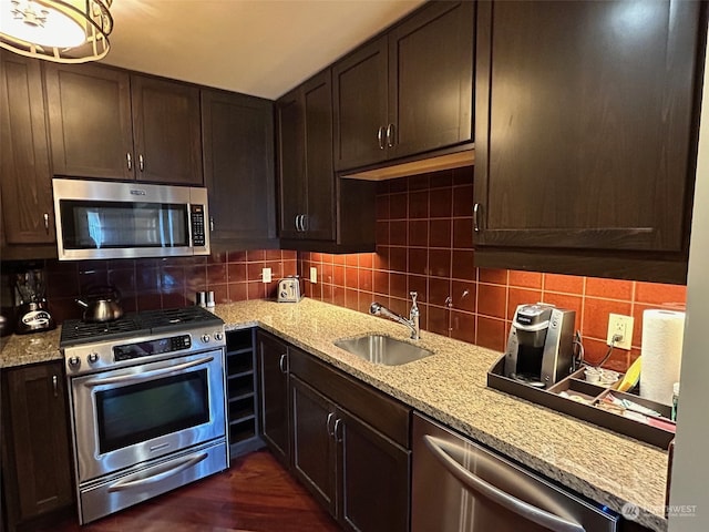 kitchen featuring dark brown cabinets, light stone countertops, dark wood-type flooring, sink, and stainless steel appliances