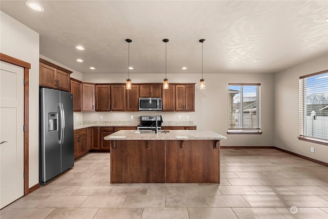 kitchen featuring a kitchen island with sink, light stone countertops, appliances with stainless steel finishes, decorative light fixtures, and a breakfast bar area