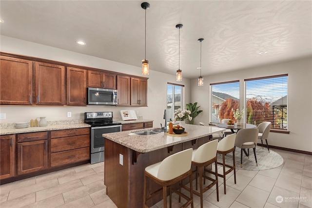 kitchen with sink, an island with sink, appliances with stainless steel finishes, decorative light fixtures, and light stone counters