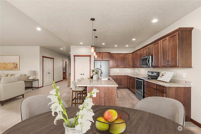 kitchen featuring light stone countertops, appliances with stainless steel finishes, light colored carpet, a center island with sink, and decorative light fixtures