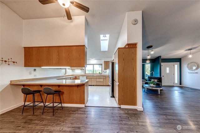 kitchen featuring lofted ceiling with skylight, a kitchen breakfast bar, kitchen peninsula, and dark hardwood / wood-style flooring