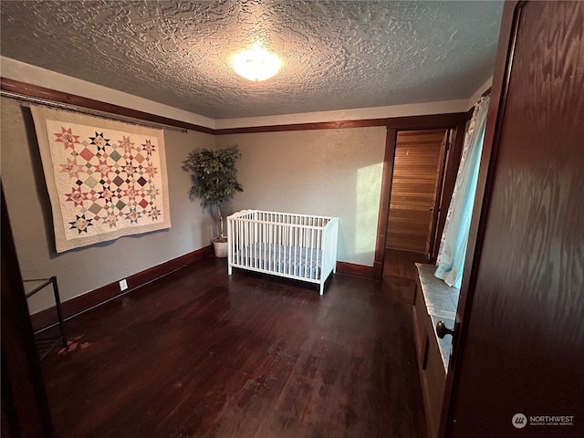 unfurnished bedroom featuring dark wood-type flooring, a nursery area, and a textured ceiling