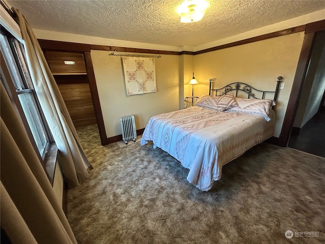 bedroom featuring radiator heating unit, a textured ceiling, and dark carpet