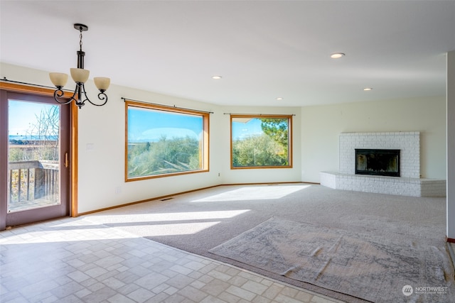 unfurnished living room featuring an inviting chandelier, light carpet, and a brick fireplace