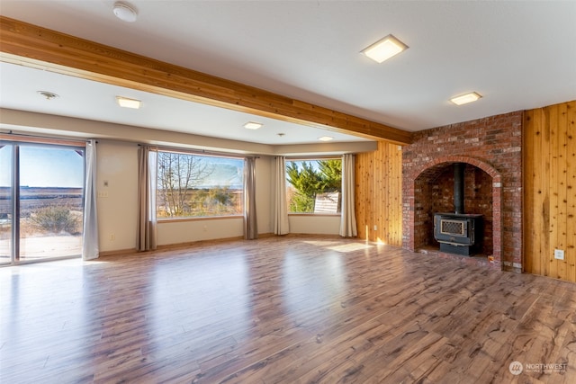 unfurnished living room featuring wooden walls, a wood stove, hardwood / wood-style flooring, and beam ceiling