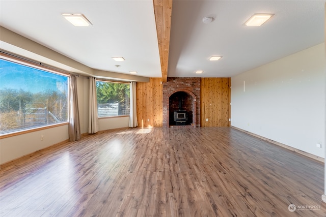 unfurnished living room featuring hardwood / wood-style floors, beamed ceiling, wooden walls, and a wood stove