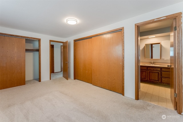 unfurnished bedroom featuring multiple closets, sink, light colored carpet, and ensuite bathroom