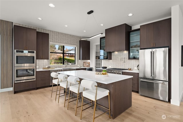 kitchen featuring a center island, tasteful backsplash, a breakfast bar, appliances with stainless steel finishes, and light wood-type flooring