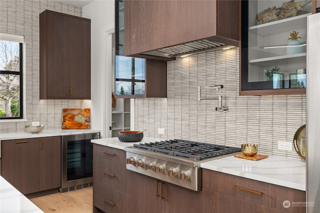 kitchen featuring light wood-type flooring, backsplash, custom range hood, beverage cooler, and stainless steel gas stovetop