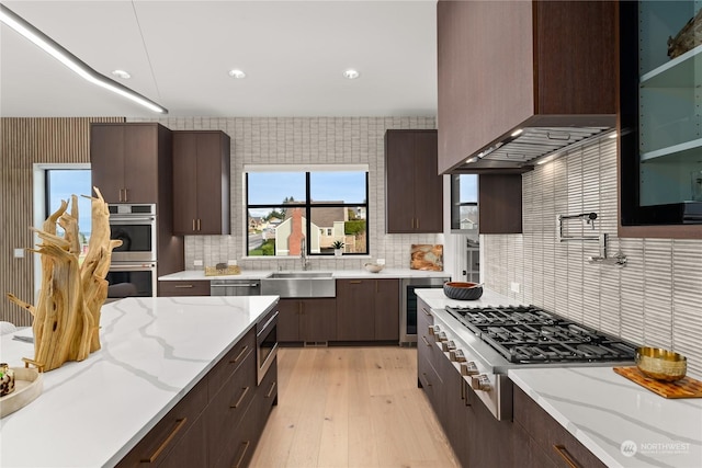 kitchen featuring sink, wall chimney exhaust hood, tasteful backsplash, light stone counters, and stainless steel appliances